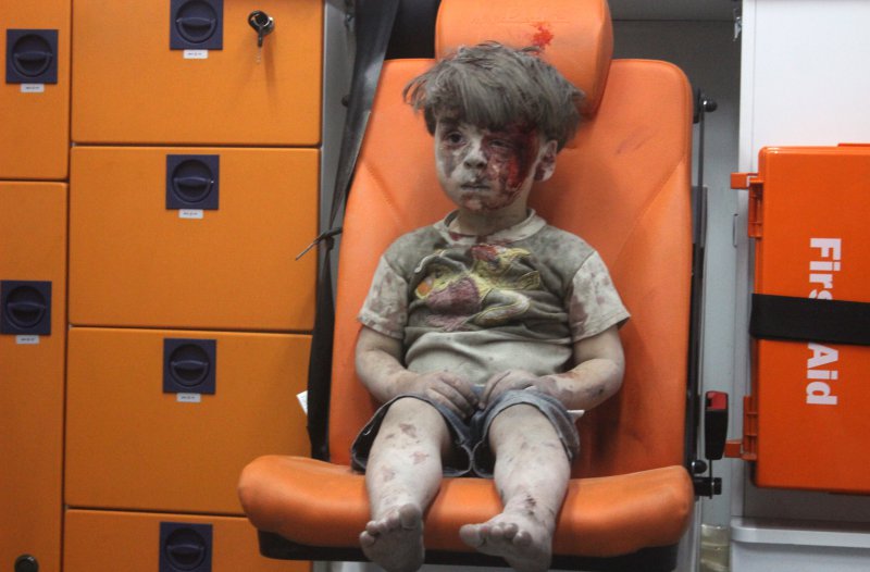 ALEPPO, SYRIA - AUGUST 17:   (EDITORS NOTE: Image contains graphic content.) 5-year-old wounded Syrian kid Omran Daqneesh sits alone in the back of the ambulance after he got injured during Russian or Assad regime forces air strike targeting the Qaterji neighbourhood of Aleppo on August 17, 2016. (Photo by Mahmud Rslan/Anadolu Agency/Getty Images)