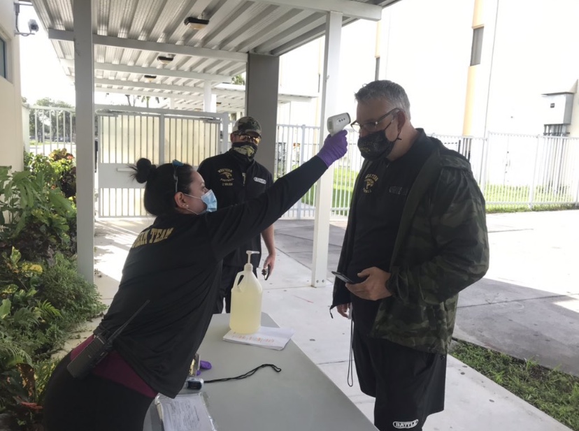 Athletic trainer Rebecca Martinez, checks head football coach Adam Ratkevichs temperature before a practice. 